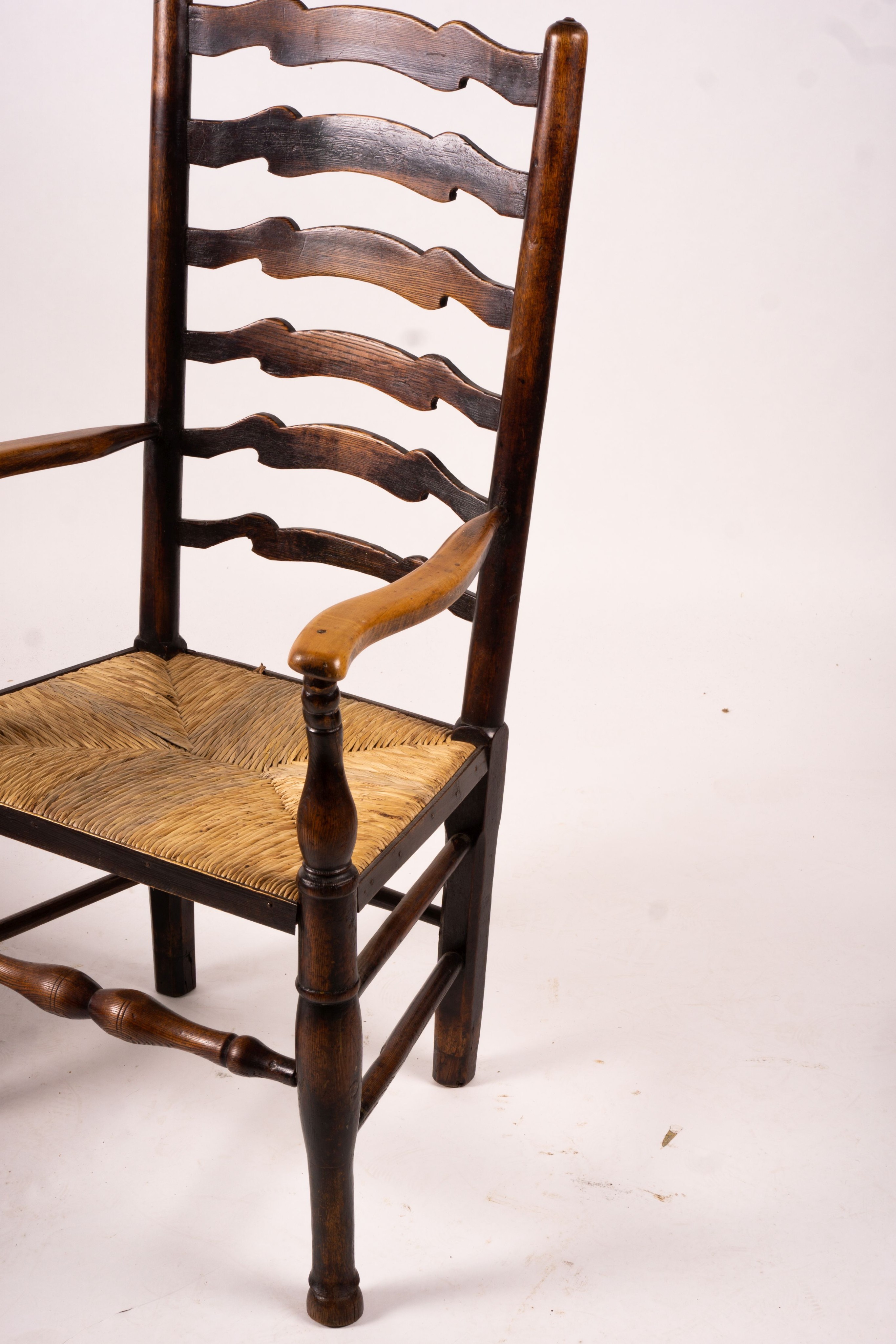 A pair of early 19th century Lancashire ash and fruitwood rush seat ladderback elbow chairs, width 60cm, depth 46cm, height 110cm